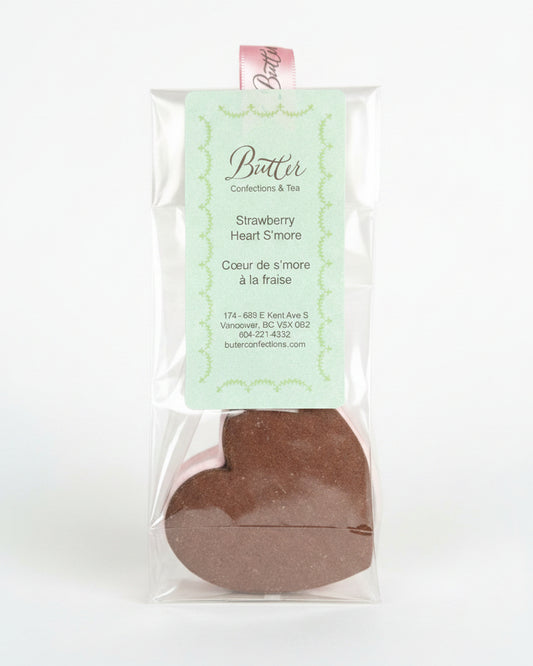 A clear plastic bag containing a heart-shaped chocolate s'more with a pale pink filling and a mint green 'Butter Confections & Tea' tag.