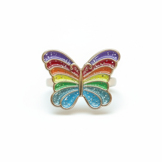 A butterfly-shaped ring with rainbow-colored enamel stripes, presented inside a pink box with a white insert printed with the brand name 'Great Pretenders'.